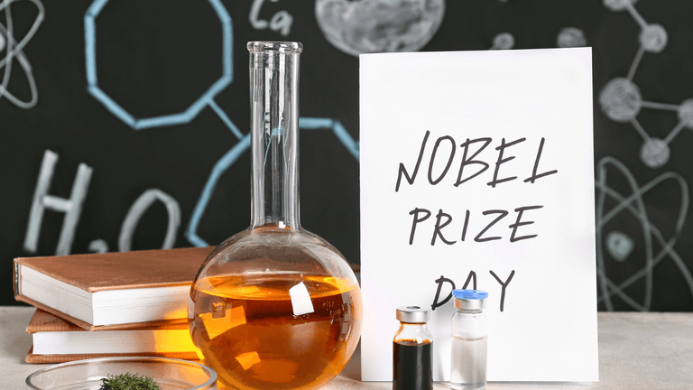 A laboratory setup featuring glassware, a sign reading Nobel Prize Day, and books.