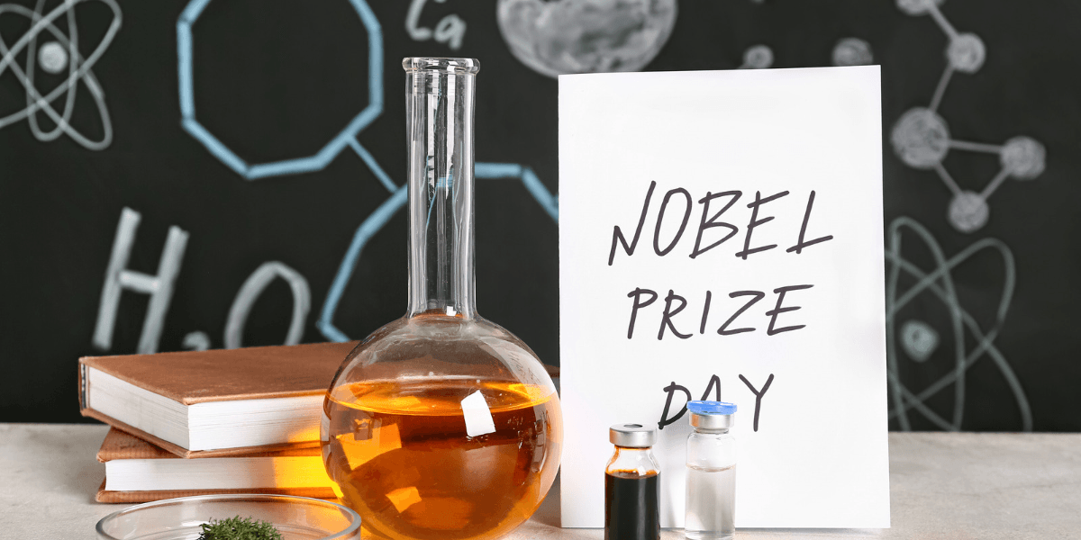 A laboratory setup featuring glassware, a sign reading Nobel Prize Day, and books.